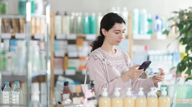 Young woman buyer scanning qr code for box of ointment in pharmacy 