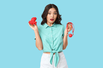 Beautiful young shocked Asian woman with mouth gag and rope on blue background