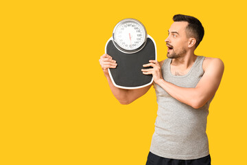 Handsome sporty shocked man with scales on yellow background. Weight loss concept