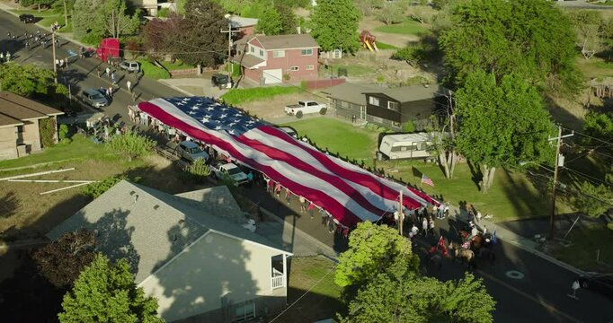 Large group of people parading massive American flag through neighborhood street - cinematic drone shot