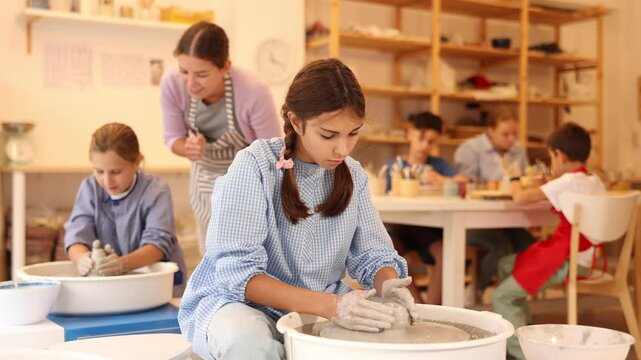 Pleased underage attendees of pottery circle working at throwing-wheel with female instructor