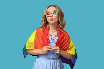 Beautiful young woman in decorative eyeglasses with LGBT flag and candy canes on blue background. Christmas celebration