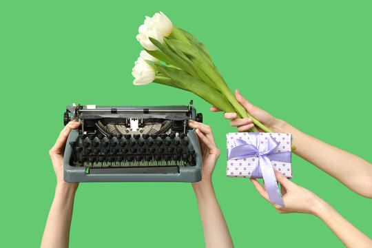Female hands with retro typewriter, gift and tulip flowers for International Women's Day on green background, closeup