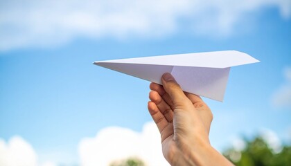 Close up photo of hand hold a white paper airplane with a blue sky background