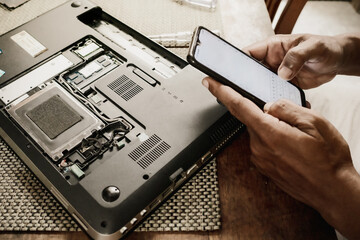 A man trying to repair his broken laptop by searching for guidance from the internet using...