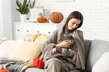Obraz premium Young woman with warm plaid and grey cat on sofa at home