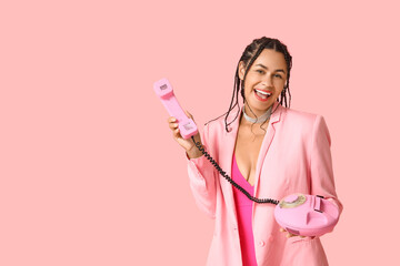 Stylish young African-American woman with dreadlocks holding retro telephone on pink background