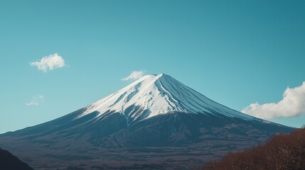 Fototapeta premium A snow-capped mountain peak stands tall beneath a clear blue sky with scattered clouds.