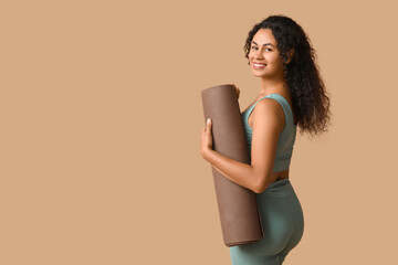 Sporty young African-American woman with yoga mat on brown background