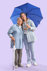 Happy senior woman and her granddaughter with umbrellas on purple background