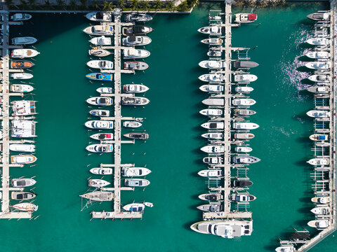Aerial view of luxury yachts docked at marina. Top-down drone shot of yachts. Boats and sailboats line the scenic seashore. Yacht cruising along the coastline. Harbor filled with vessels at dawn.