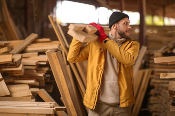 Male carpenter carrying wooden planks at sawmill