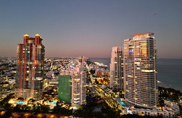 Obraz premium Miami Beach sunset aerial view. Downtown Miami skyline at dusk. South Beach neon lights at night. Tropical Miami waterfront panorama. Ocean Drive Art Deco buildings. Aerial view of Miami coastline.