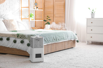 Interior of bedroom with  commode, folding screen and modern humidifier on floor near bed