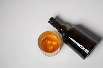 Bottle and glass of rum with ice cubes on white background
