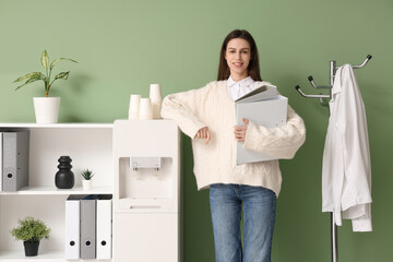 Beautiful young businesswoman with folders near modern water cooler in stylish office