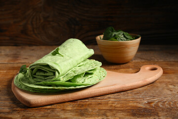 Board with fresh green lavash and bowl of spinach on wooden background
