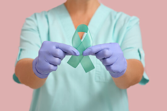 Mature female doctor with teal ribbon on pink background, closeup. Cervical Health Awareness Month