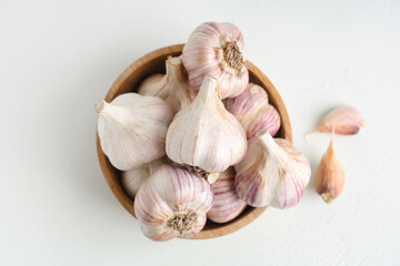 Wooden bowl with fresh garlic and cloves on white background