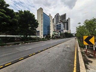 Empty city road with modern buildings and trees under cloudy sky.