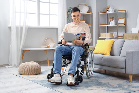 Handsome young man in wheelchair reading magazine at home