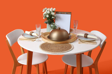 Restaurant table for two with cloche, flowers and menu on orange background
