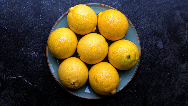Fresh lemons juicy yellow citrus fruit on dark plate - Powered by Adobe