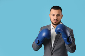 Young businessman with boxing gloves on blue background. Knockout concept