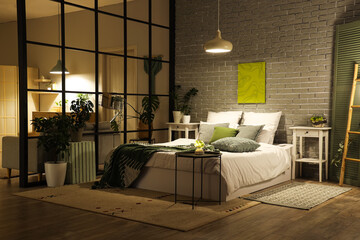 Obraz premium Interior of cozy bedroom with comfortable bed, glowing lamps and green plaid at night