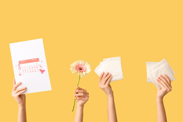 Female hands with menstrual pads, flower and calendar on yellow background