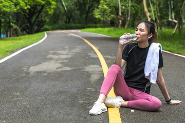 Asian sportswoman drinking water after doing exercise in nature park