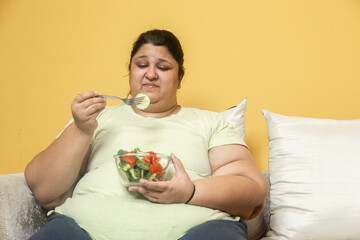 Unhappy Overweight fat indian woman eating healthy vegetable salad food at home. Plus size female dieting struggle to lose weight. Obesity concept.