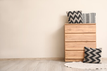 Commode with decorative pillows and rug near light wall in room