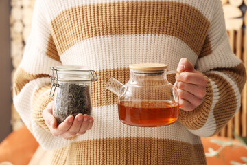 Young man holding jar of dry tea and teapot at home, closeup
