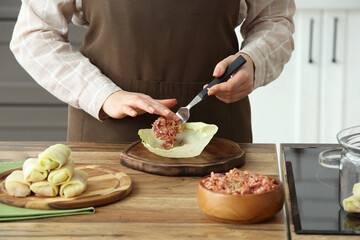Woman preparing stuffed cabbage roll at table in kitchen, closeup