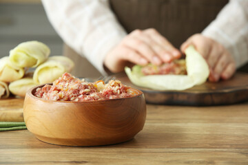 Bowl of mince on table against woman preparing stuffed cabbage rolls in kitchen, closeup