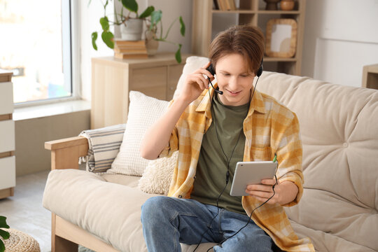 Teenage boy with tablet computer and headset working online at home