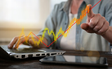 Person analyzing stock market trends on a laptop while pointing at a rising graph in a well-lit...