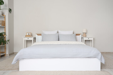 Cozy bed with grey blanket and soft pillows in stylish bedroom