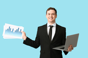 Happy young businessman with laptop and diagrams on blue background