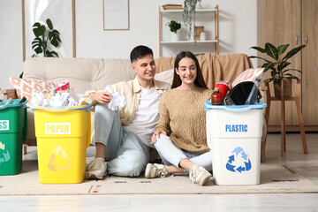 Young couple with sorted rubbish in garbage bins sitting on floor at home. Global Recycling Day