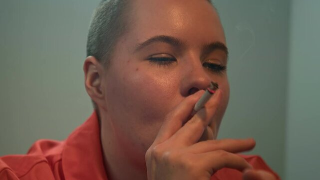 Close up shot of female Caucasian inmate in orange clothes smoking cigarette indoors