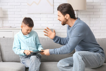 Young father and his little son with laptop squabbling on sofa at home