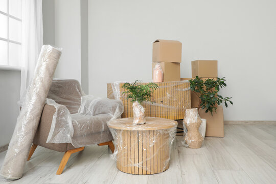 Wrapped furniture with stretch film, plants and boxes in room on moving day