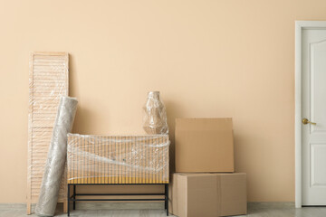 Wrapped furniture with stretch film and boxes near beige wall in room on moving day