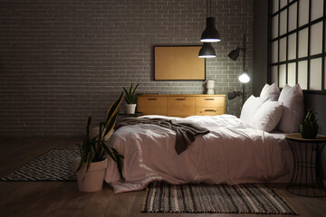 Interior of modern bedroom with cozy bed and glowing lamps at night