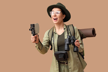 Surprised young female tourist with binoculars and photo camera on beige background