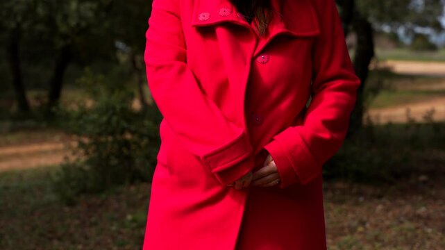 Pregnant woman stands in forest path while unbuttoning red coat to reveal belly