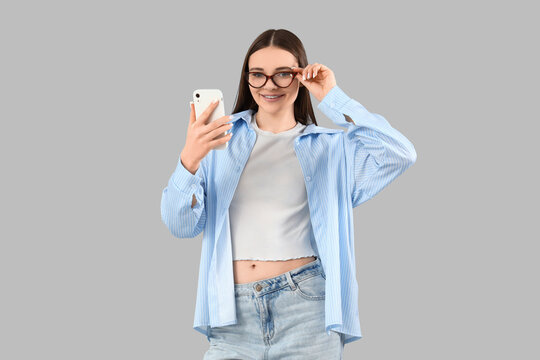 Fototapeta Young woman in eyeglasses with mobile phone on light background