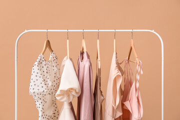 Beautiful female dresses hanging on rack against color wall, closeup